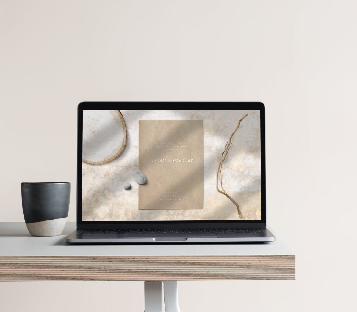 A laptop screen showing a brown online wedding invitation that includes a piece of wood, rock and stick 